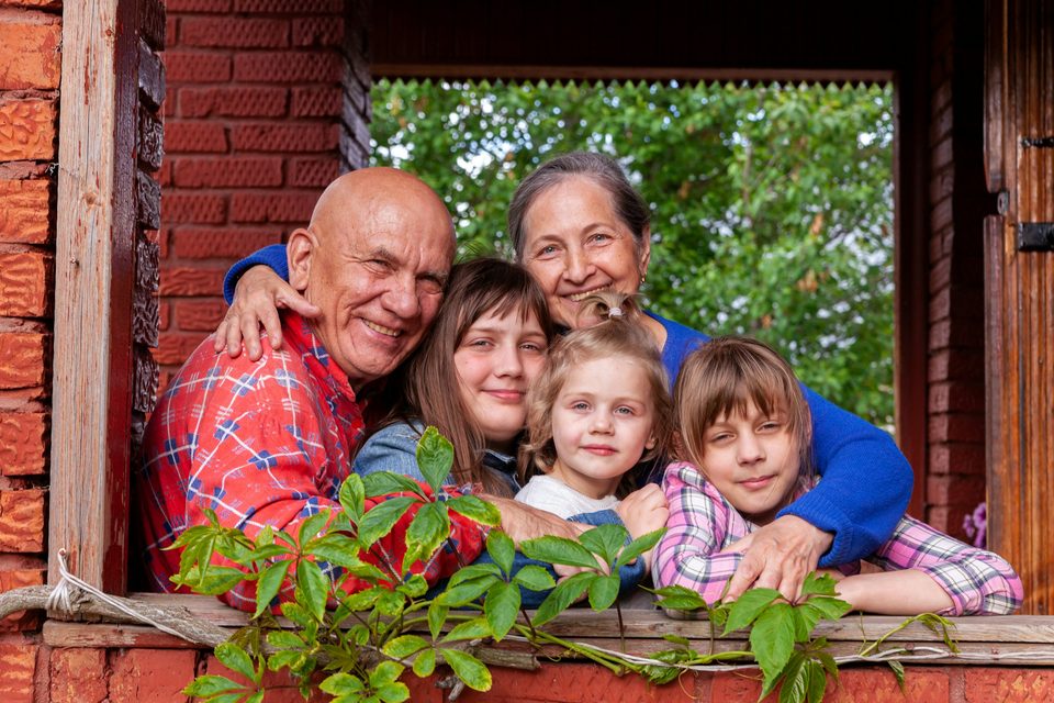 Unos abuelos abrazan a sus nietos asomados a la ventana de su casa